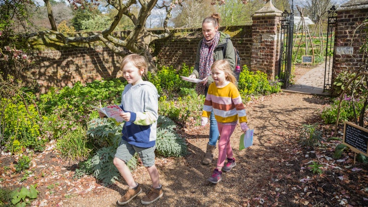 Woman and two young children walking through walled garden with Easter Trail packs